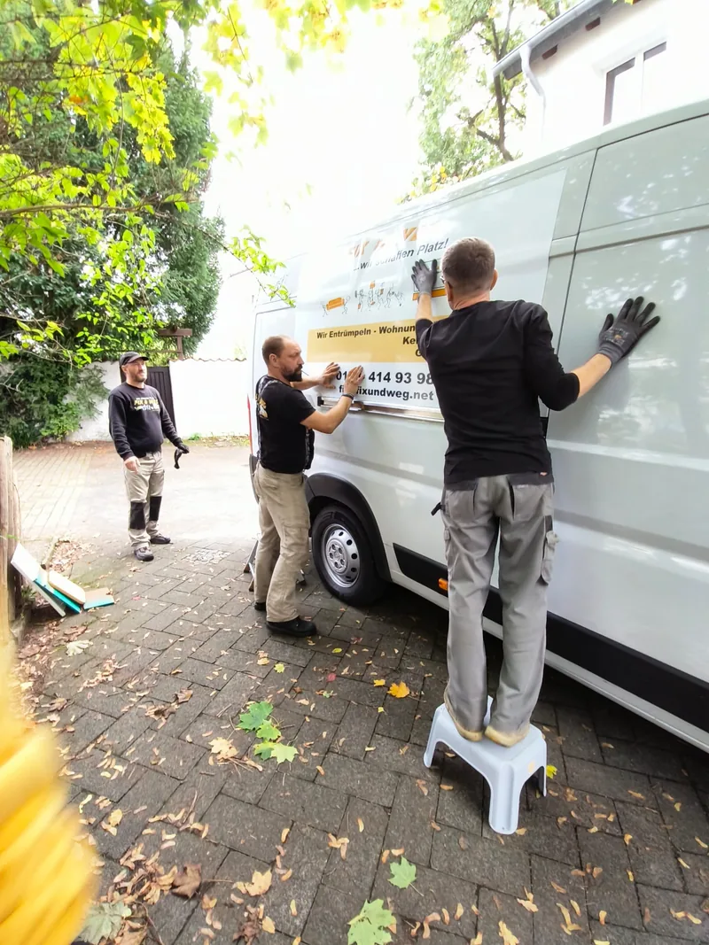 Mitarbeiter bekleben den Transporter mit dem Fix-und-weg-Schriftzug