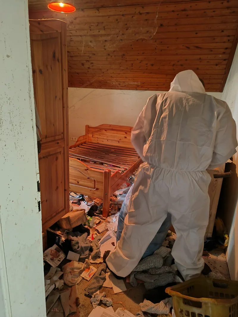 Mitarbeiter im Schutzanzug räumt ein vermülltes Schlafzimmer