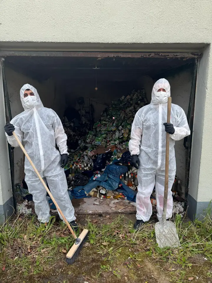 Zwei Mitarbeiter in Schutzanzügen mit Besen und Schaufel vor der vollen Garage