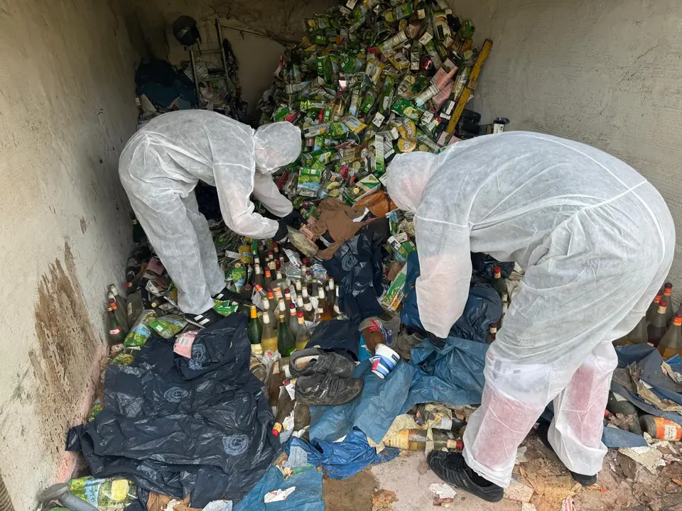 Zwei Mitarbeiter in Schutzanzügen sortieren Flaschen und Kartons in der Garage